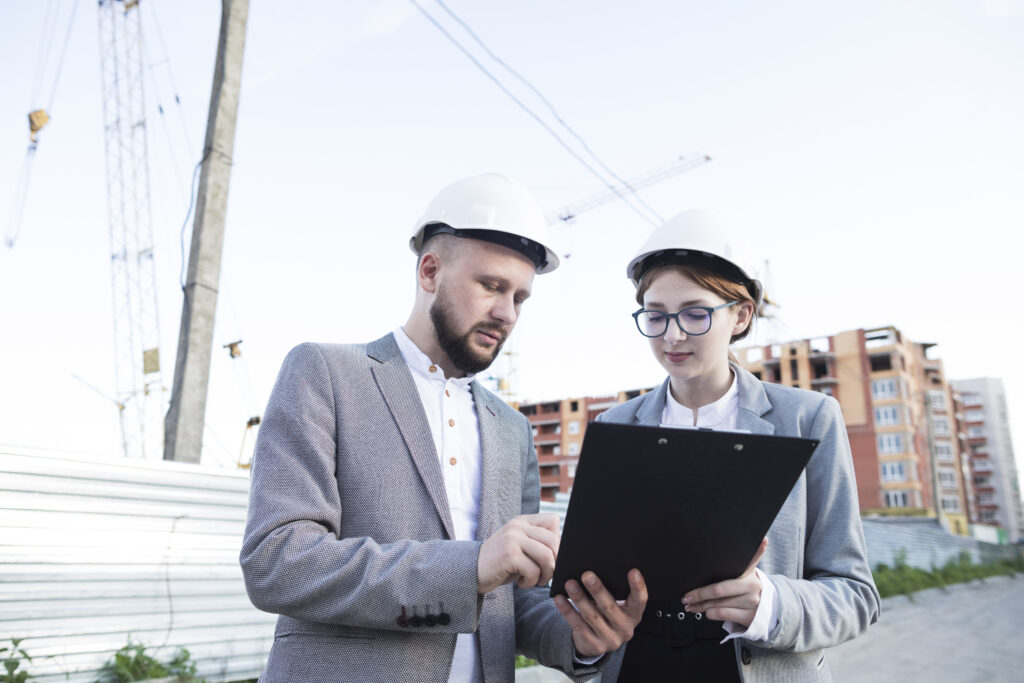 young female male architect wearing hard hat looking clipboard